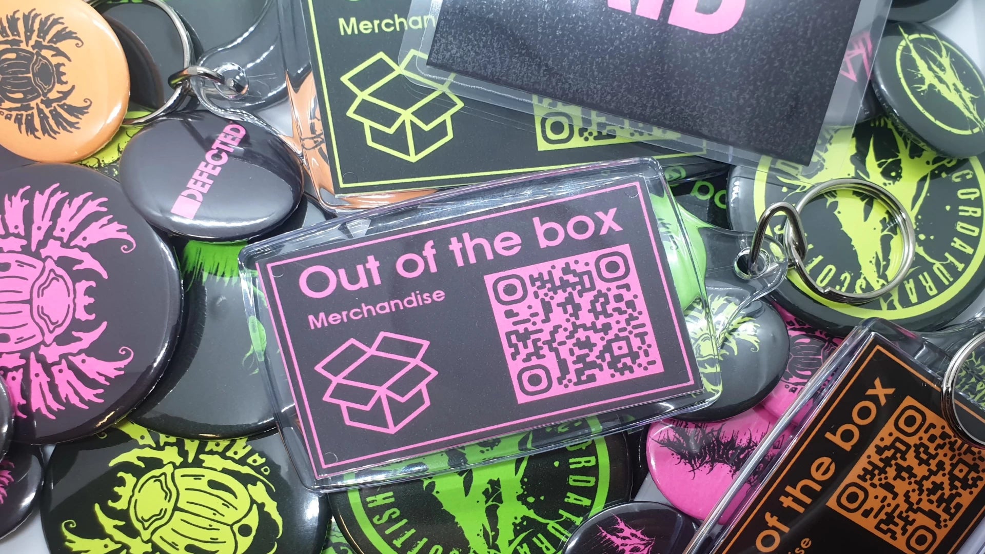 Collection of 'Out of the box' merchandise including badges and keychains with QR codes on a grey background for band merchandise.