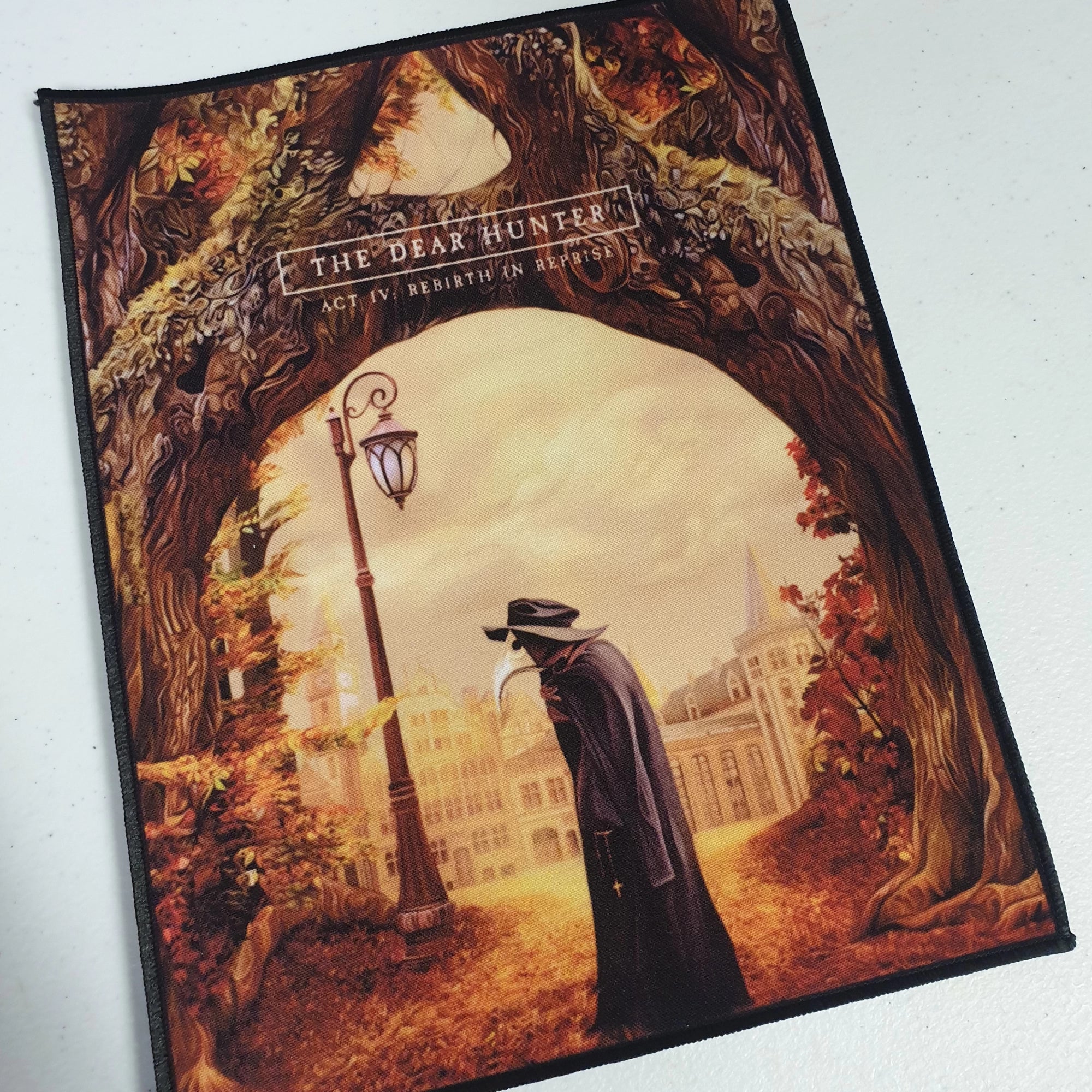 Back patch design of a person in a cloak and hat, standing under an archway with trees and a lamp post.