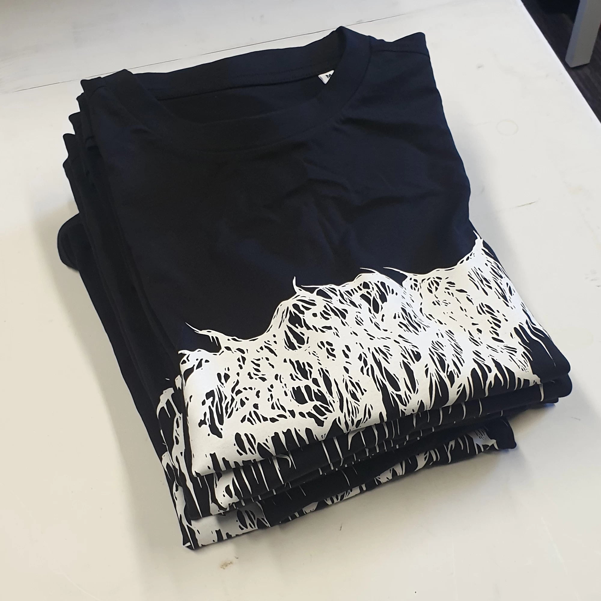 Stack of black band t-shirts with white graphic design on a white surface