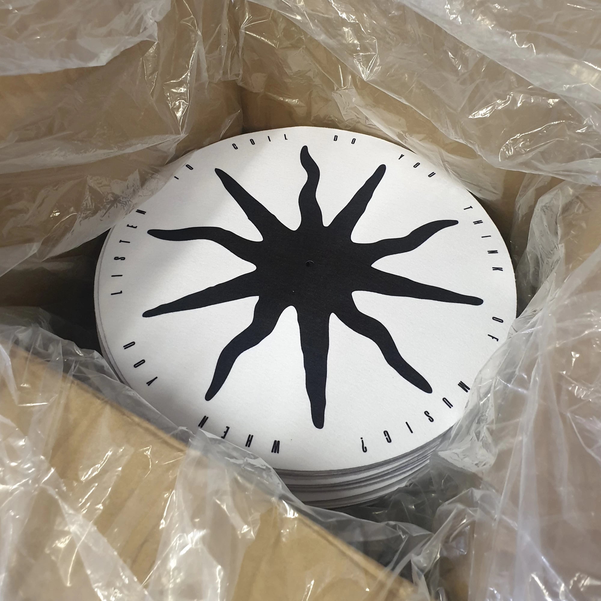 Black sun-like design on a white background, wrapped in clear plastic.