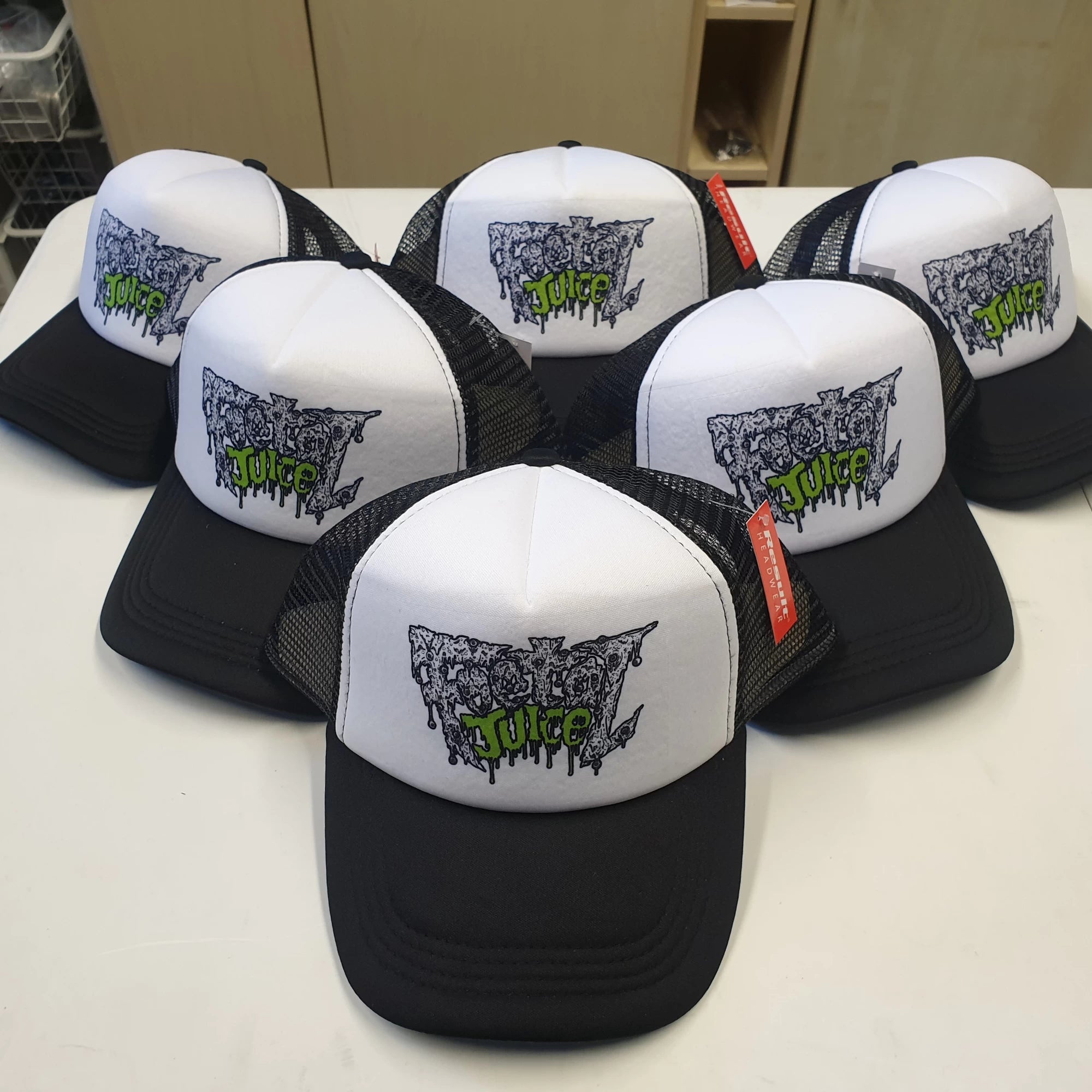 Black and white trucker caps with 'foetal Juice' band logo on a white surface
