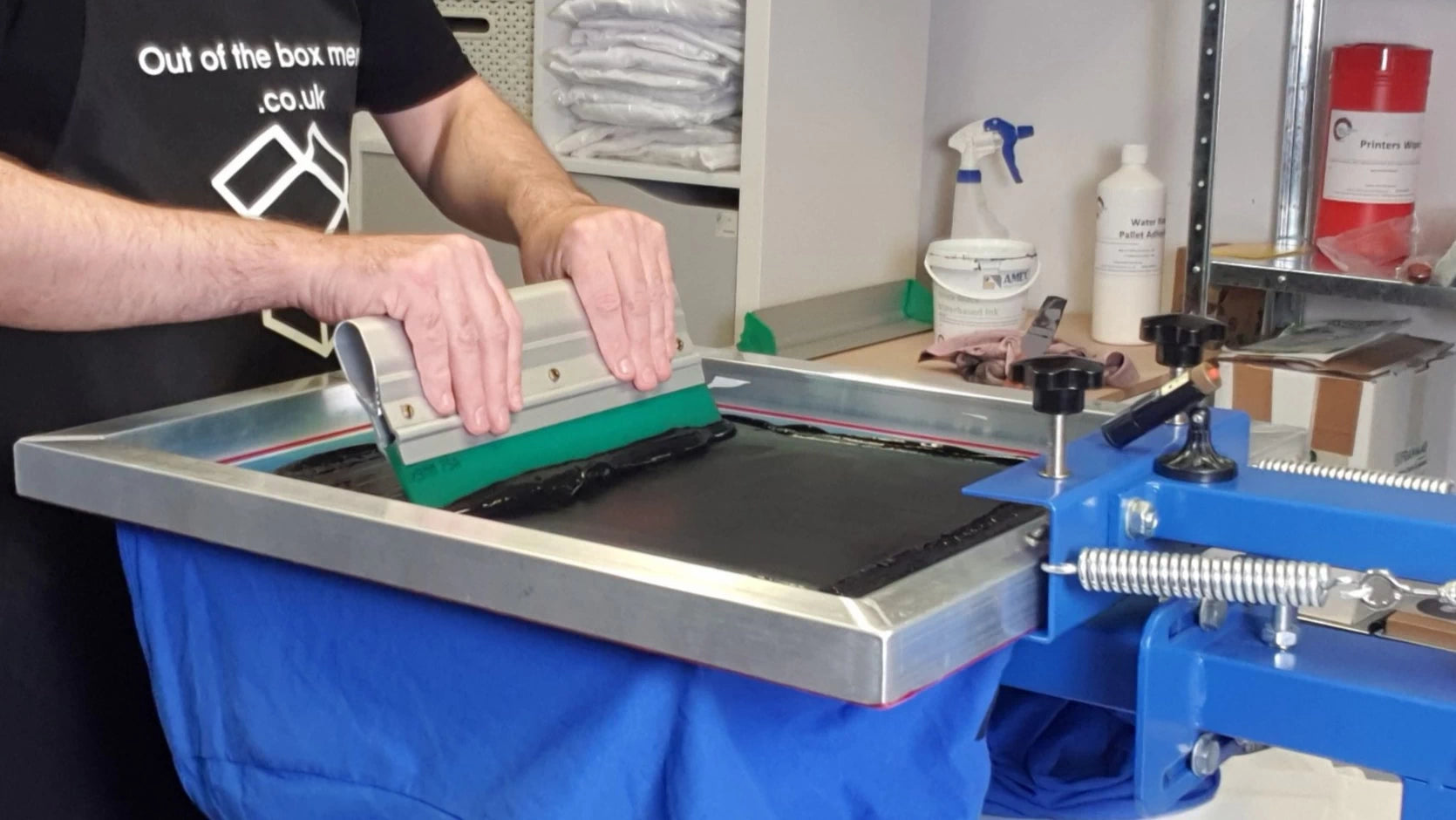 Applying black ink to a t-shirt through a silk screen in the workshop.